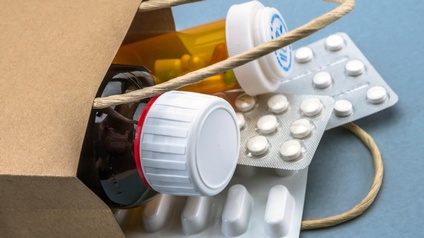 Detailansicht einer liegenden braunen Papiertasche auf blauem Untergrund aus der Medikamentenblister und Fläschchen lugen