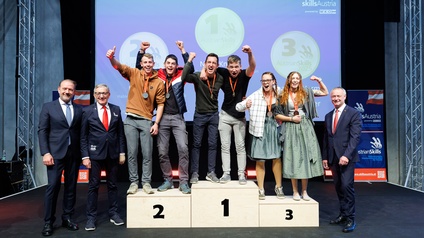 Auf einem Podesten mit den Plätzen eins bis drei stehen auf jedem Podium jeweils zwei Personen. Alle sechs Personen jubeln und haben Medaillen um den Hals. Hinter ihnen ist eine Leinwand, auf der unter anderem Gartengestalterin und skills Austria steht