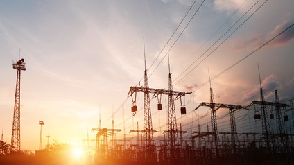 Viele Starkstrommasten unter bewölktem Himmel im Sonnenuntergang.