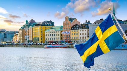 Die schwedische Flagge weht im Wind, im Hintergrund eine Stadtansicht.