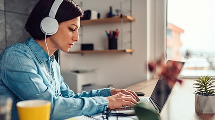 Seitenansicht. Frau mit Kopfhörern arbeitet am Laptop.