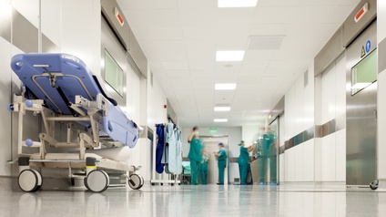 Weißer Korridor eines Krankenhauses mit Krankenhausbett und medizinischem Personal in grüner OP-Kleidung