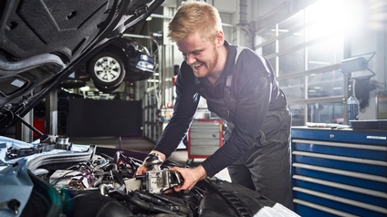 Ein junger Mann in der Werkstatt arbeitet an einem offenen Automotor