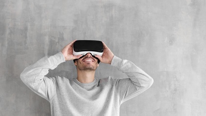 Person in hellgrauem Pullover steht vor einer 
Betonwand und trägt eine Virtual Reality Brille 