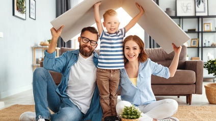 Freudige Familie in Wohnraum halten Platten über den Kopf als Symbol eines Daches, Wohnkonzept Familie