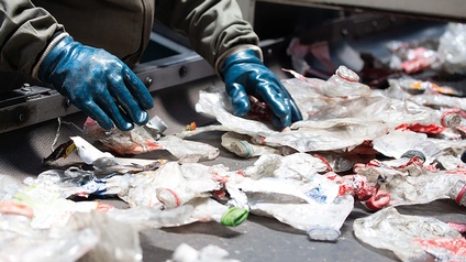 Mensch der mit Handschuhen Müll auf Förderband sortiert