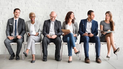 Personen in Businesskleidung sitzen auf Sesseln vor einer weißen Wand und halten freudig Unterlagen oder ein Smartphone in Händen