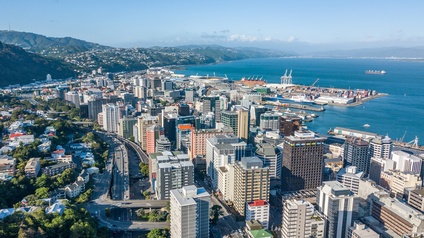Blick auf Wellington, Neuseeland, und den Central Business District, mit vielen Wolkenkratzern, Hafen, Meer und Bergkette im Hintergrund. 