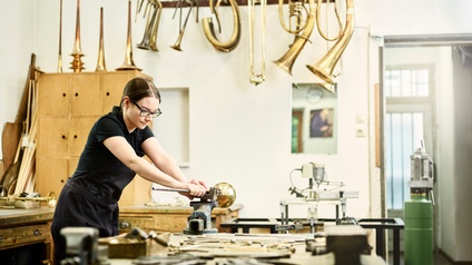 Eine junge Instrumentenbauerin arbeitet an der Werkbank an einem Blechinstrument