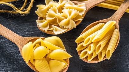 Verschiedene Pasta-Sorten sind auf Holzlöffel vor einem schwarzen Hintergrund platziert