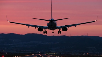 Flugzeug in Rückansicht bei Landung auf beleuchtete Landebahn im Abendrot