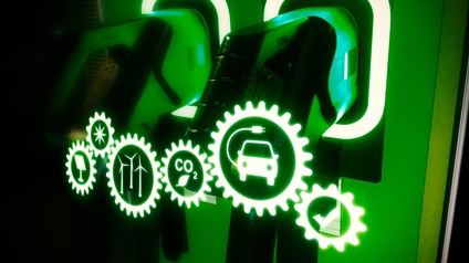 Detailansicht grünweiß leuchtender Stromzapfhähne mit Overlay von Piktogrammen zum Thema nachhaltige Energie: Häkchen, Auto mit Stromkabel, Schriftzug CO2 mit Blatt, Windräder, Sonne und Solarpanel, allesamt mit Zahnrädern umfasst