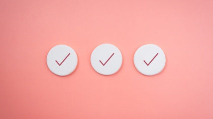 Drei weiße Scheiben mit roten Häkchen auf lachsfarbenem Hintergrund