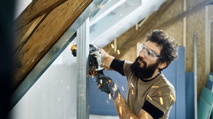 Ein Trockenbauer schleift in einem Dachboden einen Aluminiumträger für eine Zwischenwand zurecht