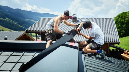 Zwei Spengler passen auf einem Dach die Blechteile ein