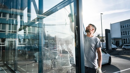 Ein Mann putzt eine weite Glasfront außen mit einem Abzieher