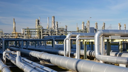 Viele Pipelines verlaufen parallel nebeneinander zu einer Raffinerie hin. Der Himmel ist blau