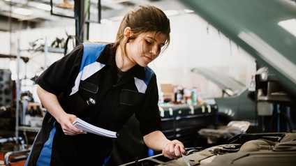 Eine Automechanikerin repariert bei geöffneter Motorhaube ein Auto.
