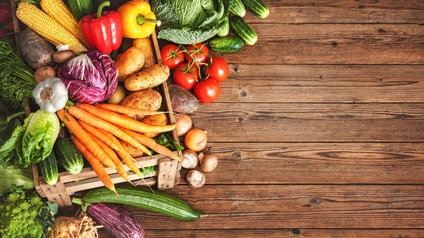 Verschiedene Gemüsesorten wie Gurken, Karotten, Kartoffel, Tomaten seitlich links drapiert auf Holzuntergrund