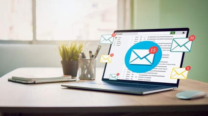 Laptop steht geöffnet auf einem Tisch und Mailbenachrichtigungen kommen rein, daneben stehen noch ein Stiftebecher, eine Zierpflanze, ein Laptop sowie eine Computermaus 