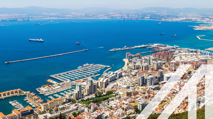Stadtansicht von Gibraltar: Im Vordergrund steil aufsteigender Bergfels, im Hintergrund Stadtlandschaft mit Hafen umgeben von Meer
