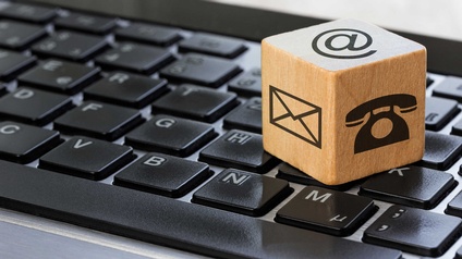 Ein Holzwürfel mit den Symbolen für E-Mail, Telefon und Postanschrift auf einer Computertastatur