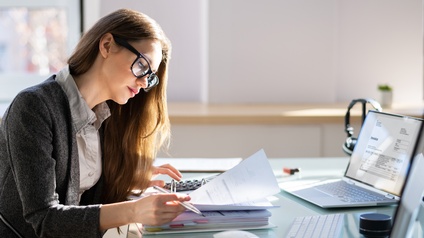 Junge Frau sitz an einem Schreibtisch und kalkuliert vor einem Laptop