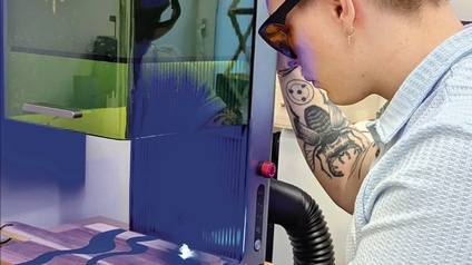 Rückenansicht einer Person mit Schutzbrille, die an einem 3D-Drucker steht