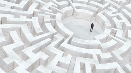 Person im Anzug steht in einem weißen Bereich eines Labyrinths, von dem aus viele Wege entspringen