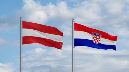 Österreichische Flagge rot-weiß-rot gestreift neben kroatischer Flagge rot-weiß-blau gestreift mit weiß-rot kariertem Wappen mittig an Fahnenmasten nebeneinander im Wind wehend, im Hintergrund blauer Himmel mit Wolken
