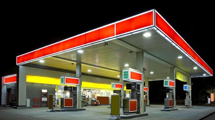 Außenaufnahme einer Tankstelle bei Nacht mit einem rot leuchtenden Dach. Unter dem Dach sechs Säulen, an jeder Säule sind Zapfhähne montiert.