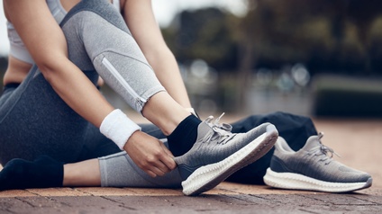 Eine Person in langer Sporthose und Oberteil sitzt am Boden im Freien und zieht sich Sportschuhe an