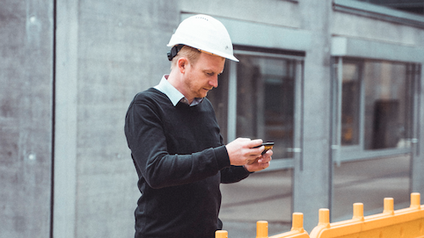 Grubinger mit weißem Baustellenhelm auf einer Baustelle, an einem Tablet arbeitend.