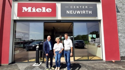 Personen stehen vor einem Gebäude mit dem Schriftzug Miele 