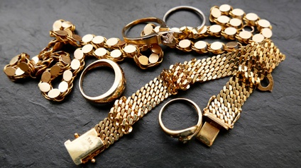 Goldschmuck wie Kette, Armband und Ringe neben- und aufeinander auf dunklem steinartigem Untergrund platziert