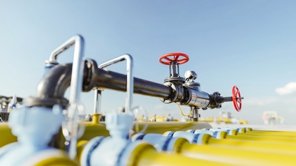 Fokus auf Gashahn mit Rohrleitungen bei einer natürlichen Gasstation mit gelben Rohren und blauem Himmel