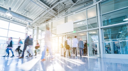 Mehrere gehenden Personen in Bewegungsunschärfe im lichtdurchfluteten Gang einer Messehalle