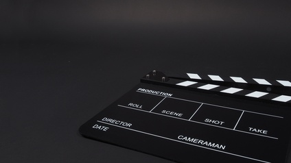 Auf schwarzem Untergrund liegt eine Filmklappe auf der steht: Production, Roll, Scene, Shot, Take, Director, Cameraman, Date