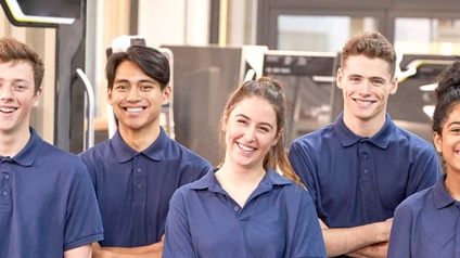 Porträt von fünf Personen. Jede Person trägt ein blaues Oberteil. Die Personen stehen in zwei Reihen. Alle haben die Mundwinkel leicht nach oben gezogen