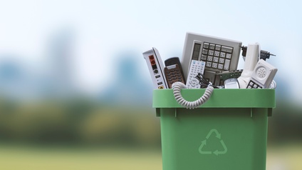 Grüne Mülltonne mit Recycling-Zeichen und entsorgten Altgeräten