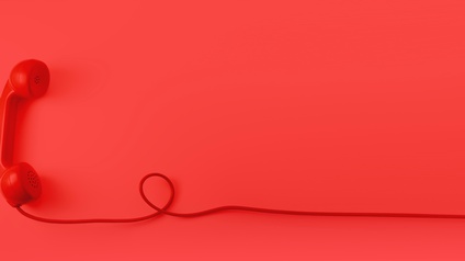 Roter Telefonhörer mit rotem Kabel eine Schlaufe bildend vor rotem Hintergrund