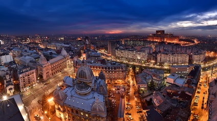 Topshot einer Stadt bei Nacht mit beleuchteten Gebäuden. Zwischen den Gebäuden sind mehrspurige Straßen, die beleuchtet sind. Auf den Straßen parken teilweise Autos