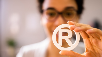 Eine Person hält mit ihrer linken Hand den weißen Buchstaben R in die Kamera, der von einem weißen Kreis umfasst wird