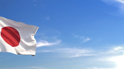 Die Flagge des Landes Japan weht an einem Mast angebracht im Wind. Im Hintergrund ist blauer Himmel mit vereinzelten Wolken zu sehen.