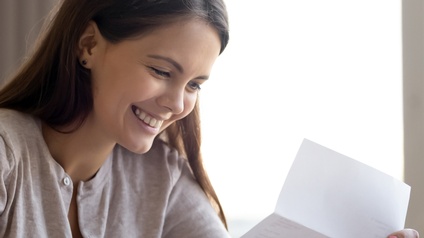 Lächelnde Person mit langen dunklen Haaren liest einen Brief