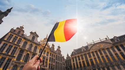 Die Hand einer Person im Ausschnitt, die die belgische Flagge schwingt, im Hintergrund historische Gebäude.