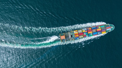 Top-Shot eines Containerschiffs auf Wasser fahrend, beladen mit vielen bunten Containern. Um das Schiff Bildung von Wellen durch die Fahrt des Schiffes