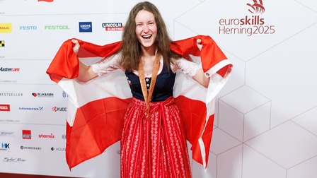 Katharina Höller, lachend, mit Medaille und Österreich-Flagge um die Schultern