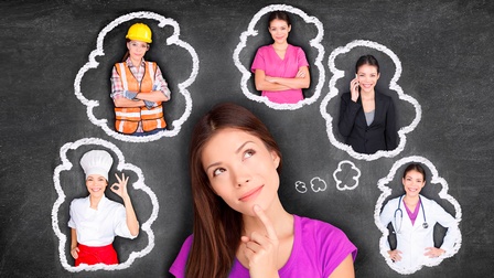 Eine junge Frau vor einer schwarzen Tafel in Nachdenk-Pose- Auf der Tafel verschiedene aufgezeichnete Gedanken-Wölkchen, in denen sie sich verschiedene Karrieremöglichkeiten wie Köchin oder Bauarbeiterin ausmalt