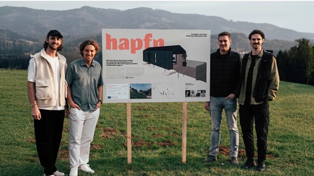 Vier Personen stehen auf einer Wiese neben einem Schild.